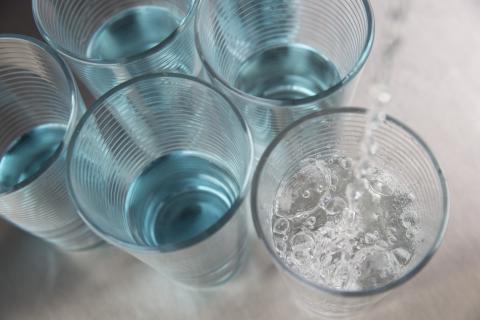 water is being poured into a glass adjacent to other half-full water glasses