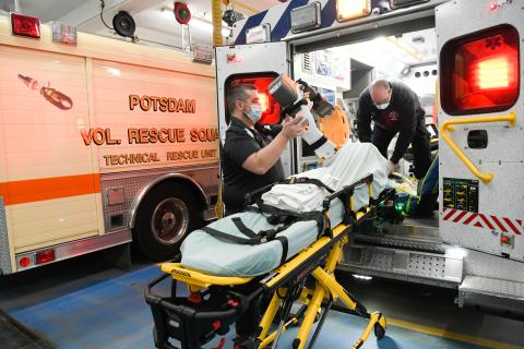 two EMTs load a gurney into the back of an ambulance.