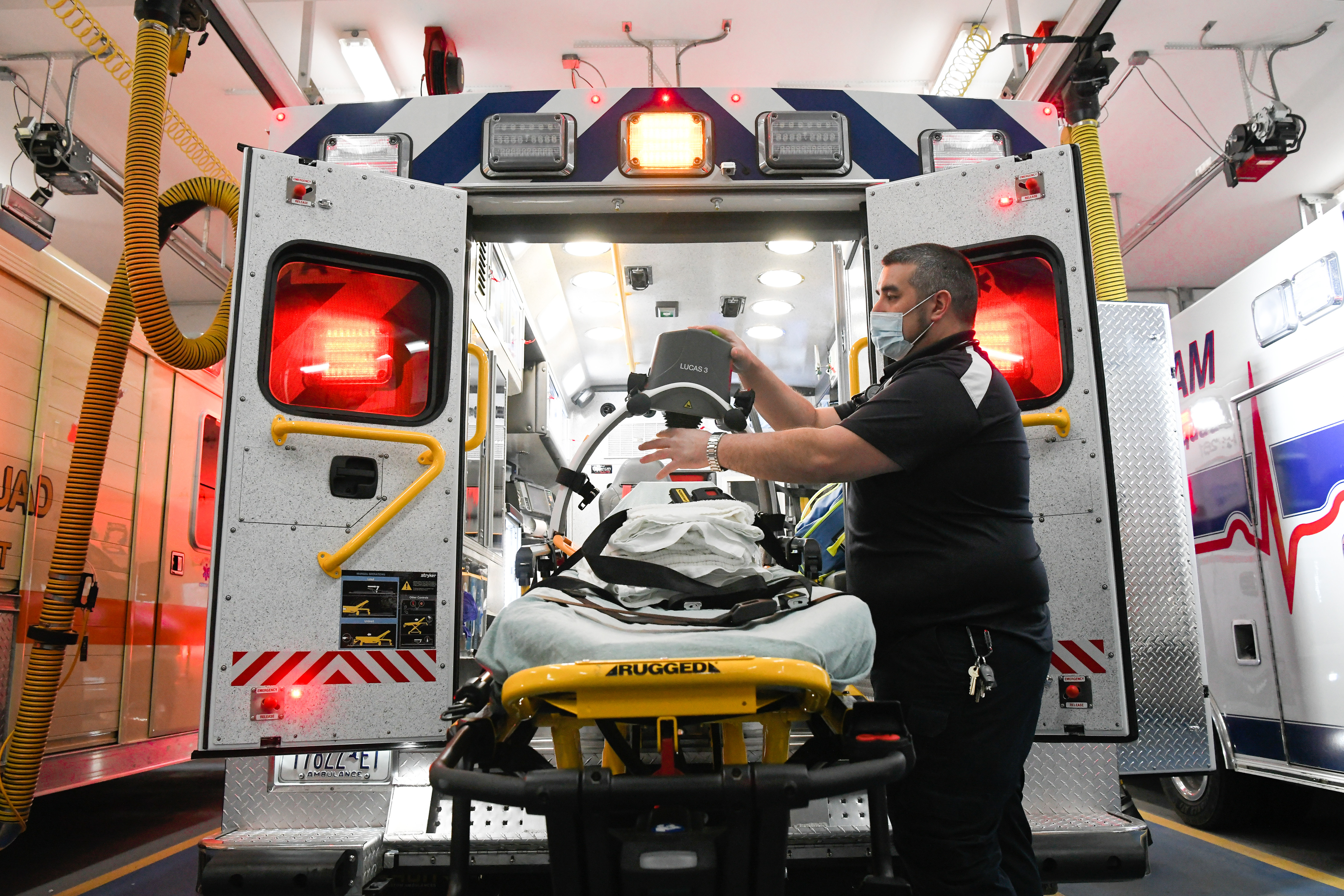 An EMT prepares a medical gurney at the back of an open ambulance.