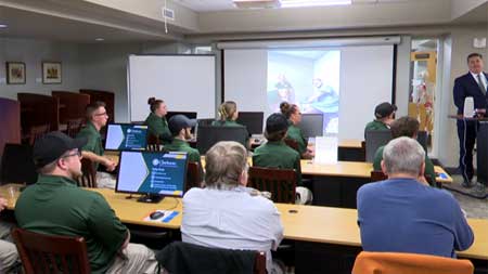 Screen grab from TV news story of paramedics sitting in a classroom with their backs to the camera watching a speaker.