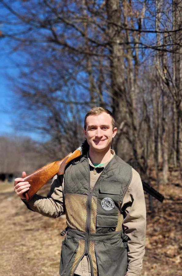 a man standing with a gun on his shoulder outside next to the woods