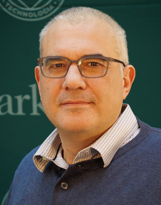 Chest-up portrait of Ioannis Mastorakos in blue button-up sweater and checkered, open-collar shirt