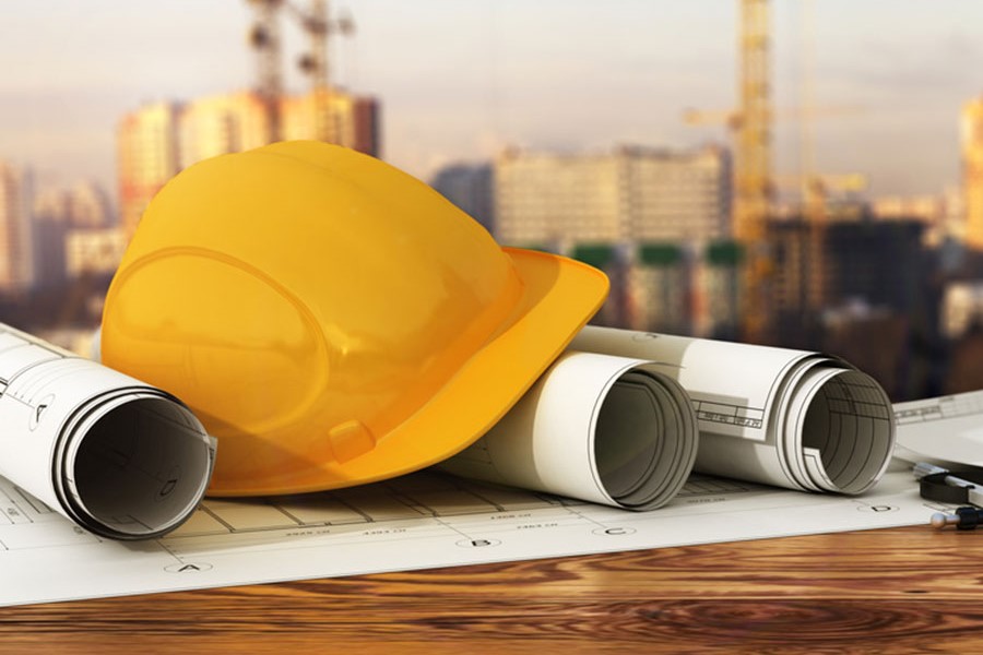 A photo of a hard hat sitting on top of blueprints in front of a construction site.