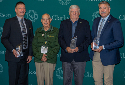 Four men standing in front of a Clarkson backdrop holding glass awards.