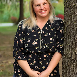 Presenter Janet Taylor leans against a tree outside