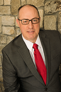 Presenter Tim Redding looks into the camera while wearing a suit and standing in front of a stone wall